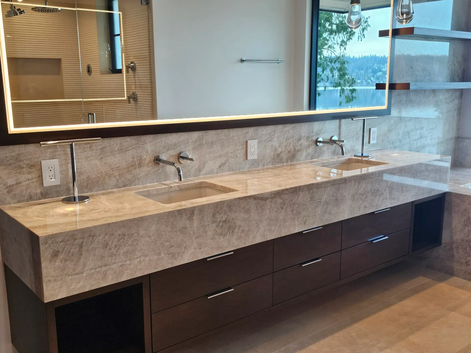 Floating taupe quartzite double vanity with thick mitred edge, wall-mount faucets, and lake view