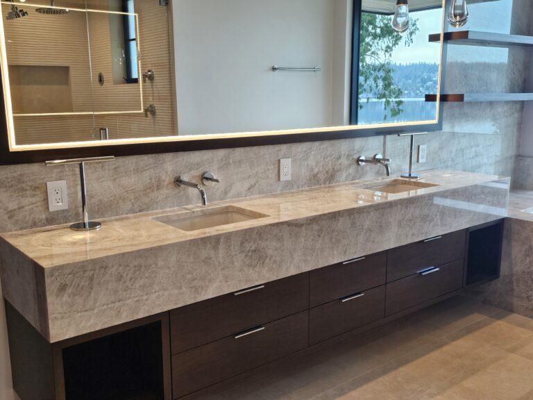Floating taupe quartzite double vanity with thick mitred edge, wall-mount faucets, and lake view