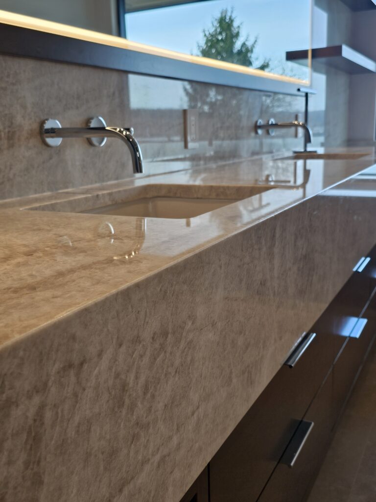 Angled detail of the quartzite vanity top and backsplash with chrome wall-mounted faucets