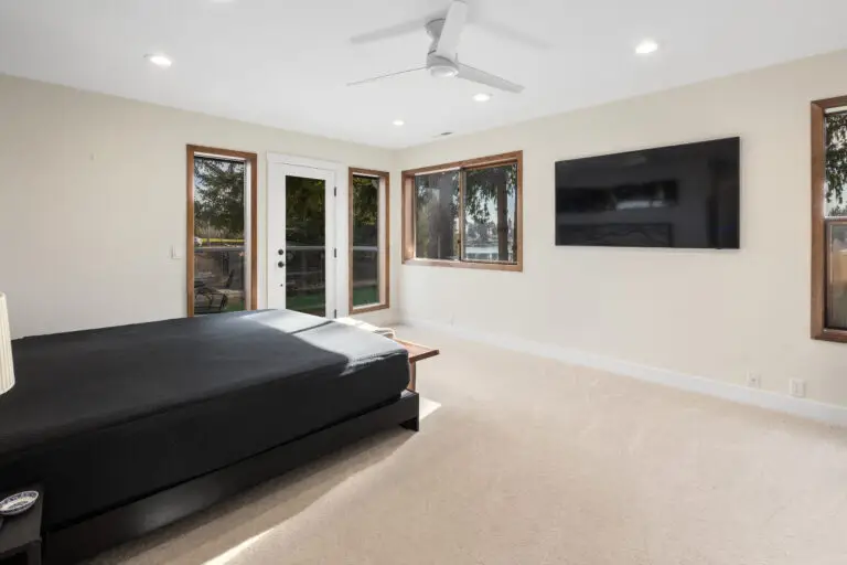 Spacious primary bedroom with platform bed, wall-mounted TV, ceiling fan, and deck access with lake glimpses