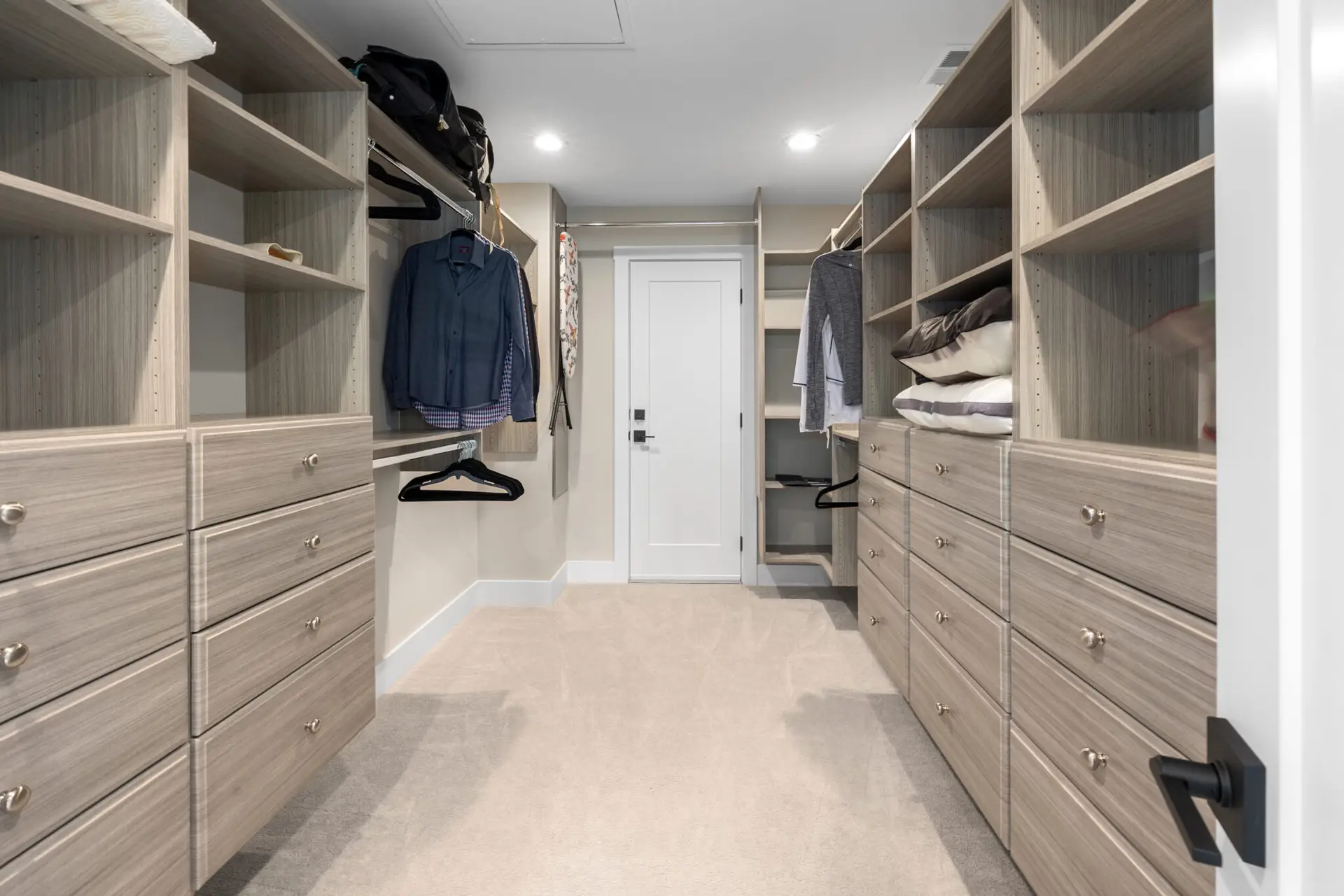 Walk-in closet with custom light wood built-ins, drawer banks, and hanging storage