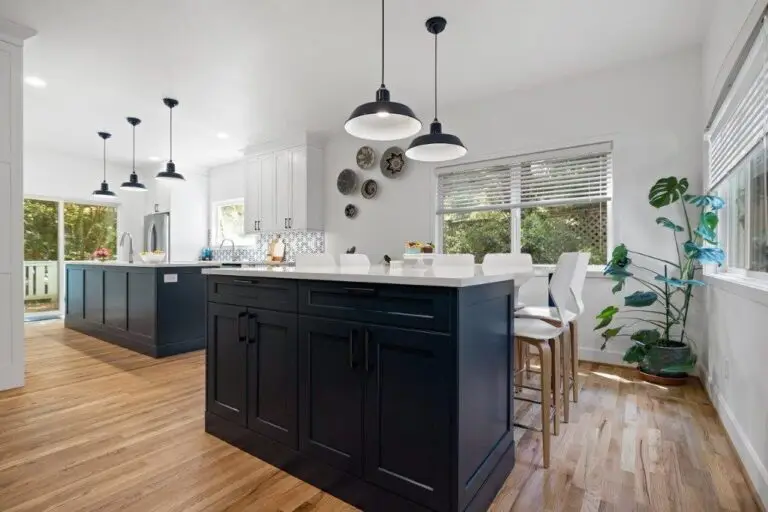 Navy island with white quartz counter under black barn pendants, corner windows and hardwood floors