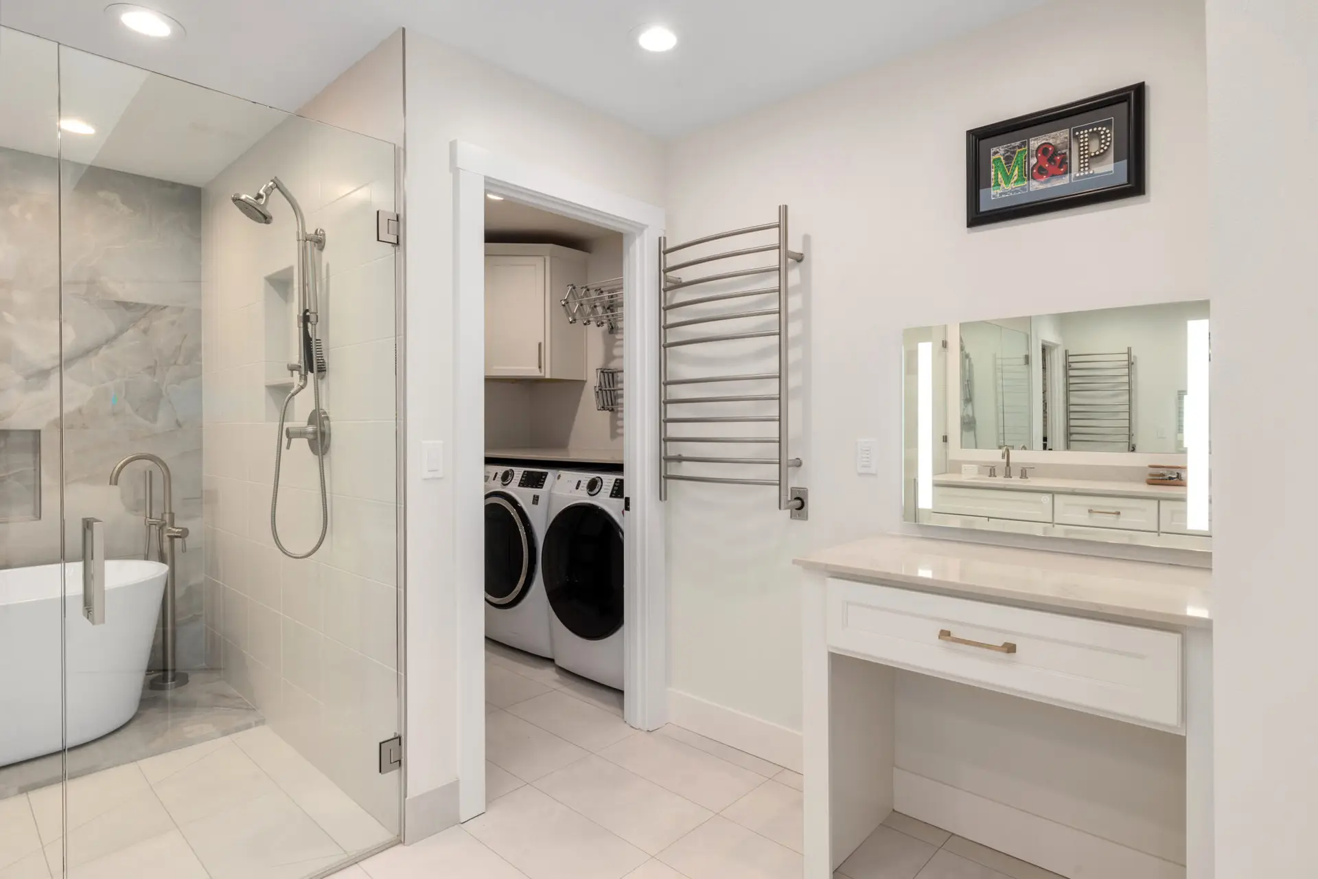 Primary bathroom with glass shower, freestanding tub, heated towel rack, and adjoining laundry room