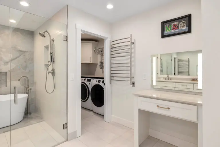 Primary bathroom with glass shower, freestanding tub, heated towel rack, and adjoining laundry room
