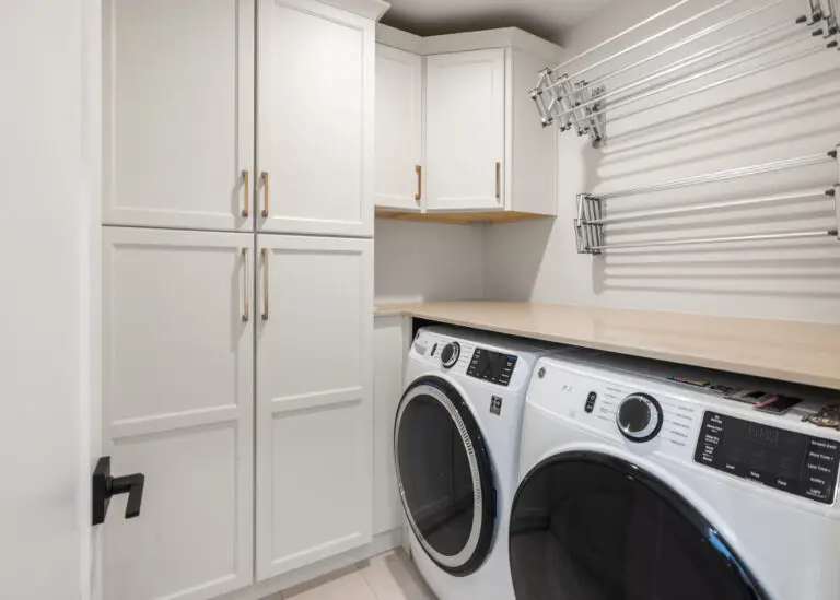 Laundry room with white cabinetry, brass pulls, wall-mounted drying racks, and front-load washer and dryer