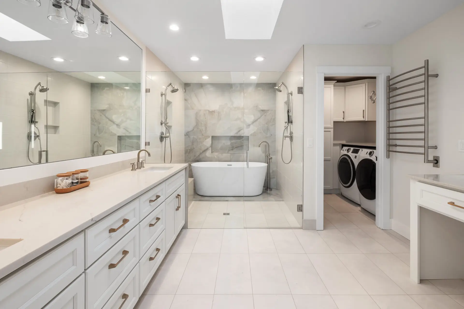 Primary wet room with freestanding tub, marble-look accent wall, dual shower stations, and makeup vanity