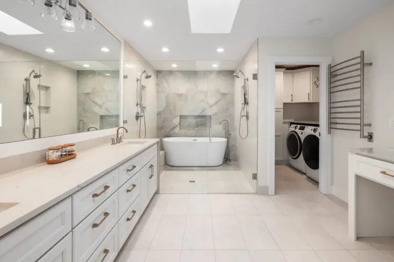 Primary wet room with freestanding tub, marble-look accent wall, dual shower stations, and makeup vanity