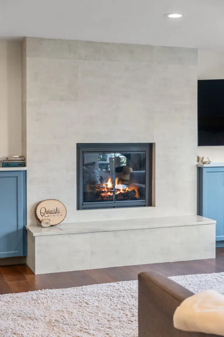 Tiled fireplace wall with floating hearth bench flanked by blue cabinets in the family room