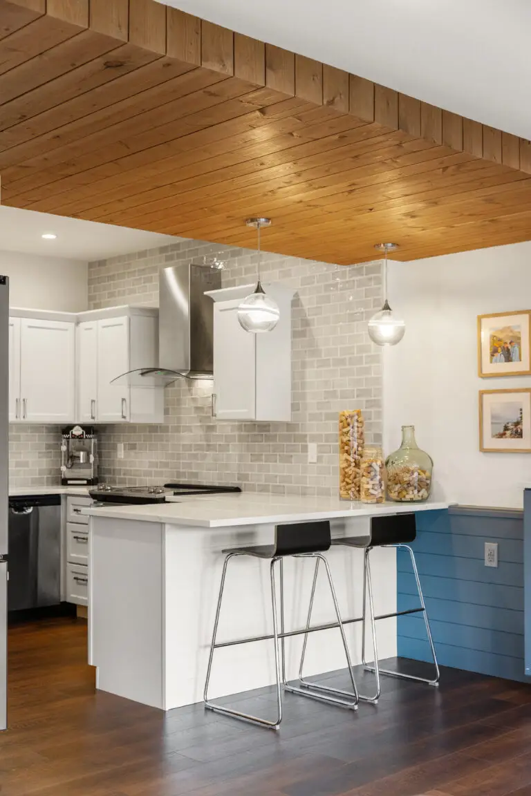 Secondary kitchen with wood plank ceiling, pendant lights, blue shiplap peninsula, and gray subway backsplash