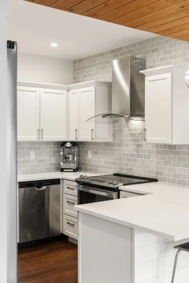 White kitchen corner with gray subway tile, curved glass range hood, and stainless appliances