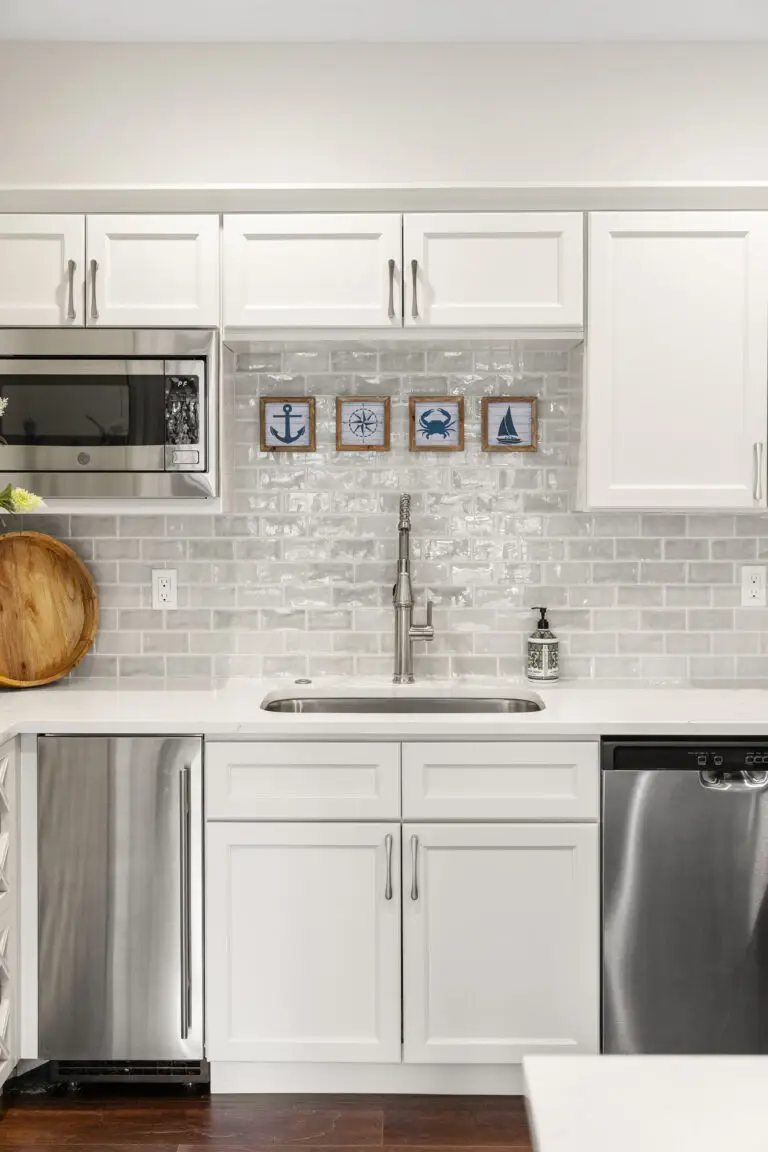 Kitchen sink wall with nautical art on glossy subway tile, stainless beverage fridge, and dishwasher