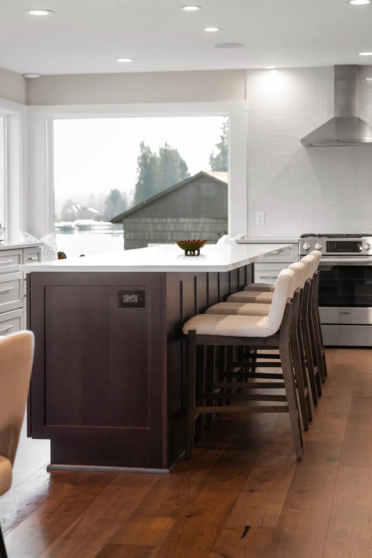 Dark wood island end with upholstered counter stools and stainless slide-in range in a lakeside kitchen