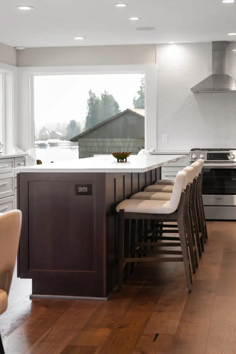 Dark wood island end with upholstered counter stools and stainless slide-in range in a lakeside kitchen