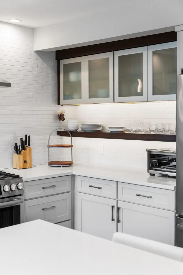 Kitchen wall with frosted glass cabinets, dark floating shelf of dishware, and under-cabinet lighting