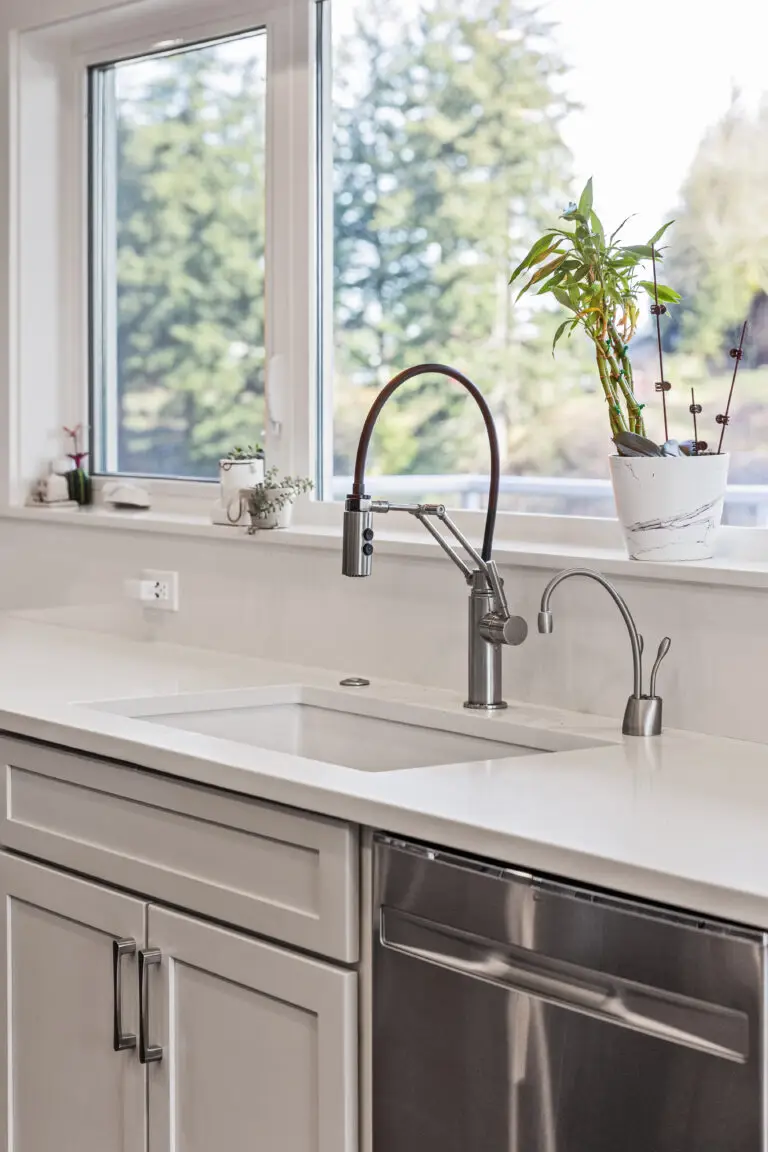 Kitchen sink detail with articulating faucet and filtered water tap beneath windows with greenery