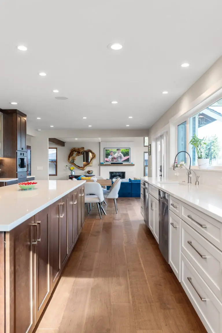 Galley view of double-island kitchen with quartz counters and wood floors opening to the living room