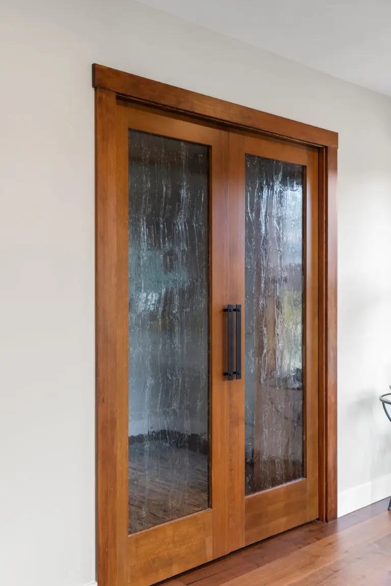 Wood-framed double pocket doors with textured rain glass and black handles in a lakeside home remodel