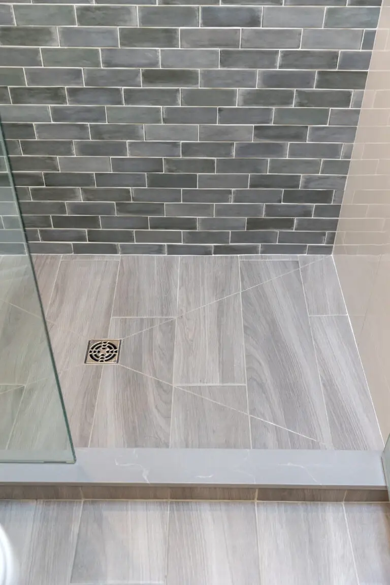 Shower floor detail with gray wood-look plank tile, square nickel drain, and gray subway tile wall