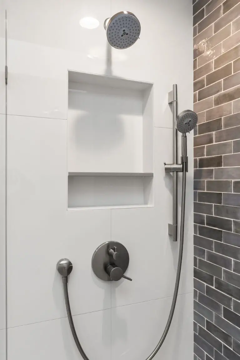 White tile shower wall with recessed niche, handheld sprayer on slide bar, and gray subway tile accent