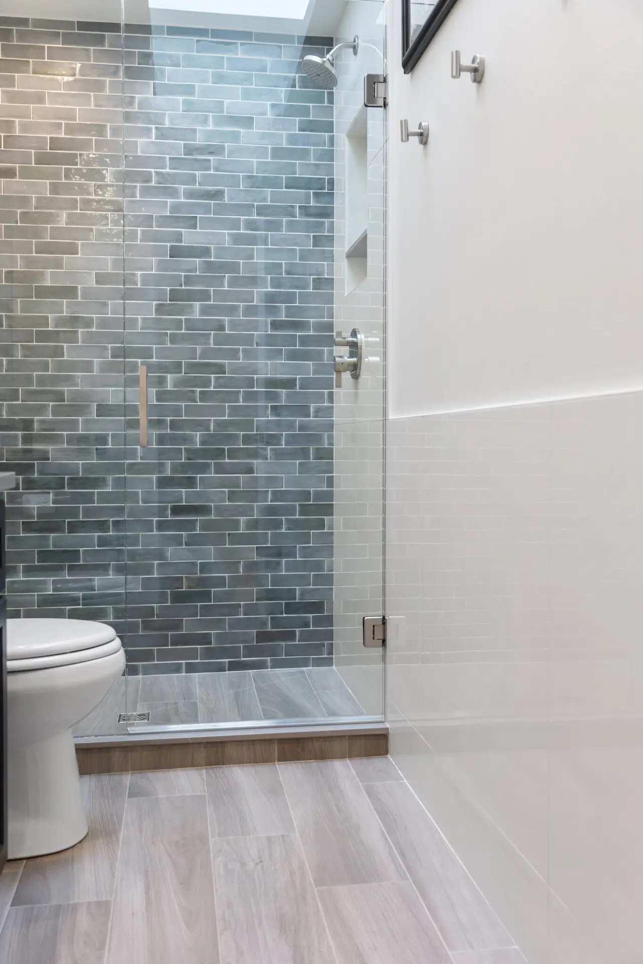 Bathroom with frameless glass shower, blue-gray subway tile accent wall, and wood-look tile floor