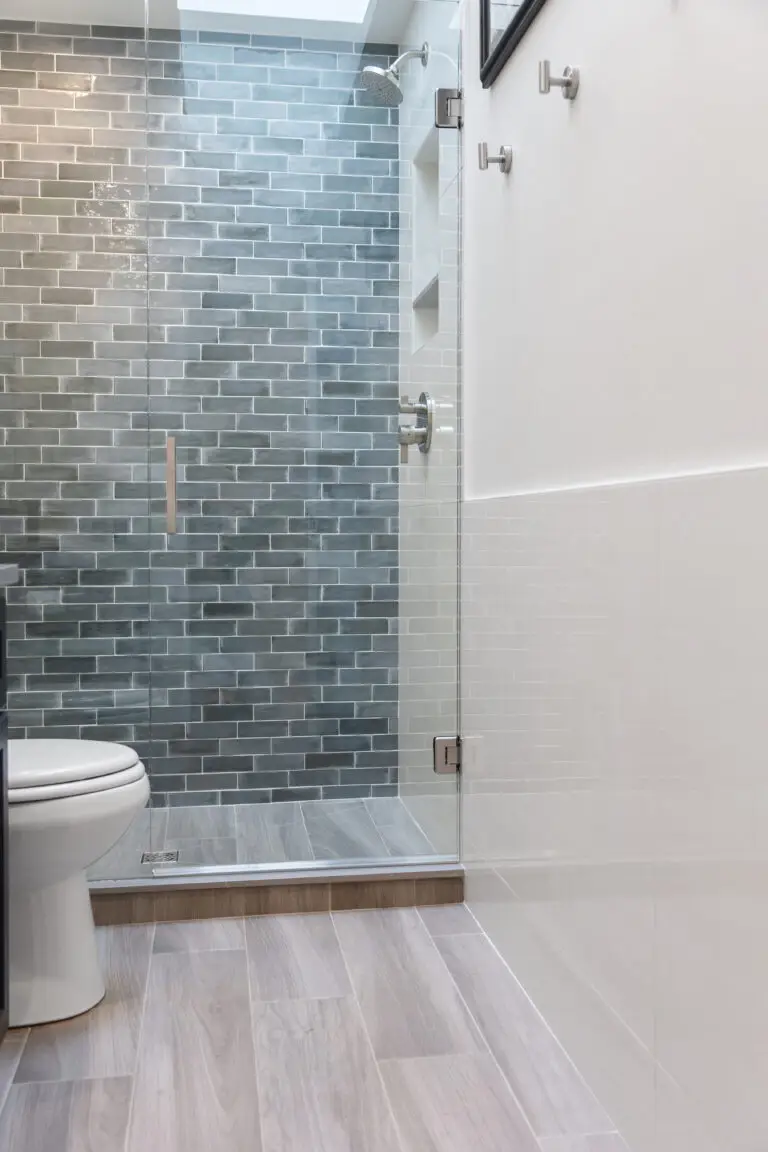 Bathroom with frameless glass shower, blue-gray subway tile accent wall, and wood-look tile floor
