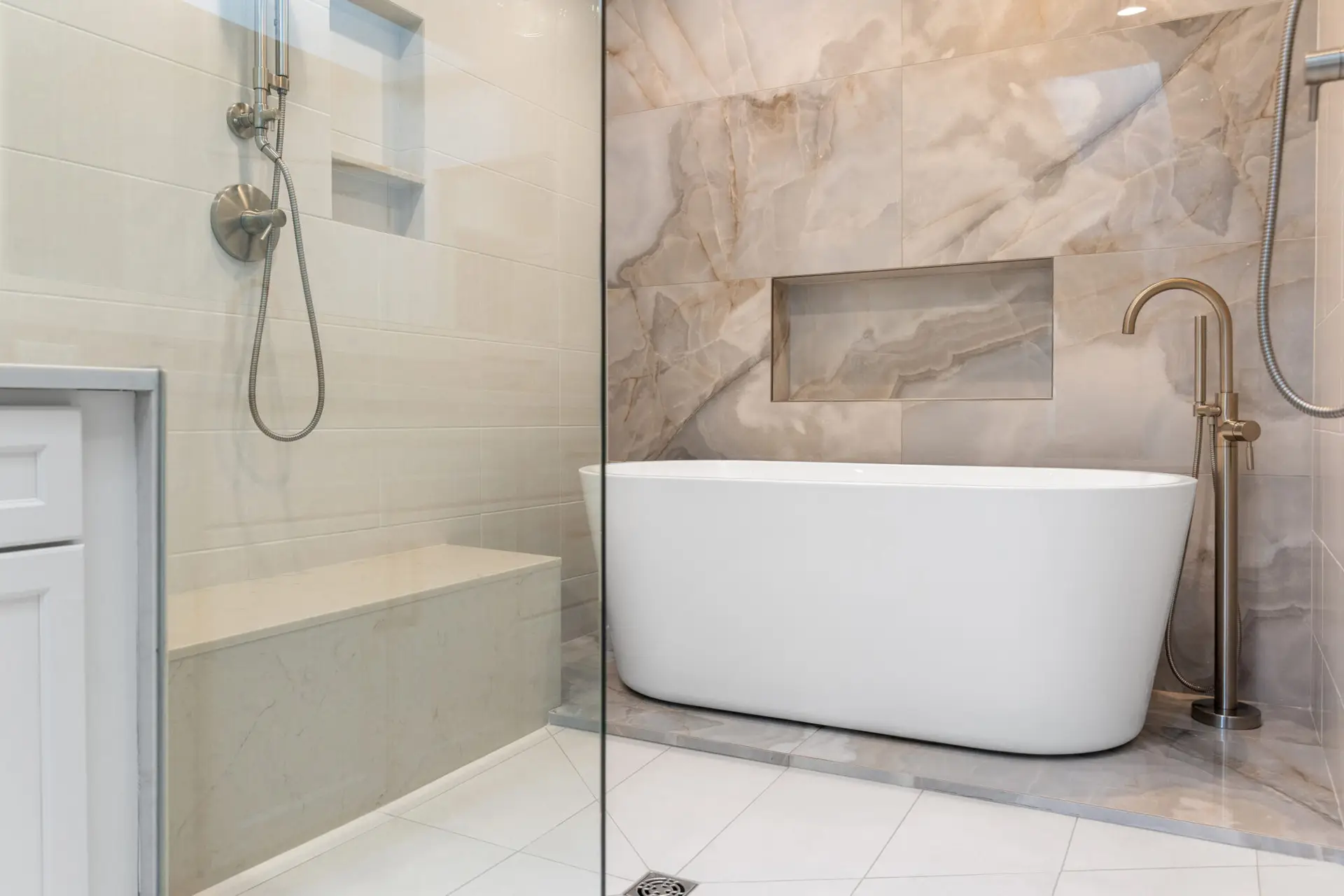 Wet room with freestanding tub, quartz shower bench, handheld sprayers, and marble-look feature wall