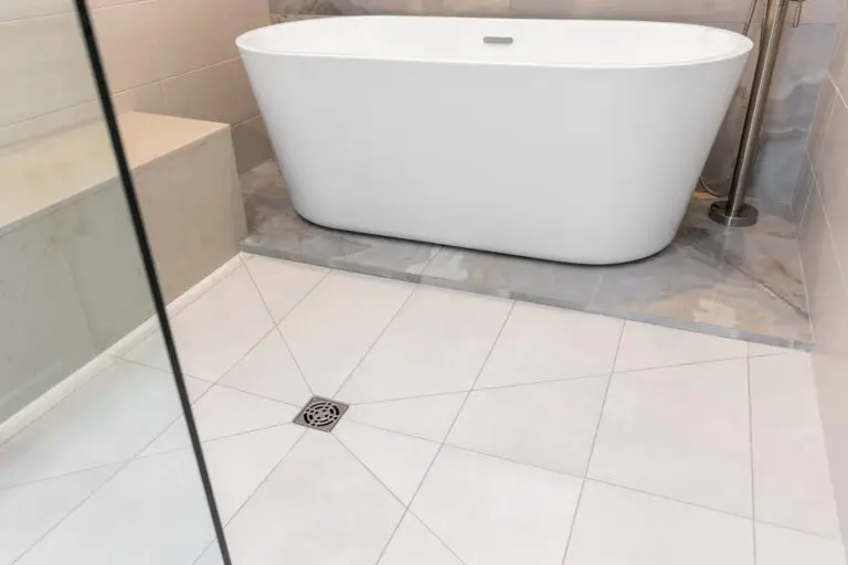 White freestanding tub on marble-look tile platform beside crisp white floor tile laid in a geometric pattern