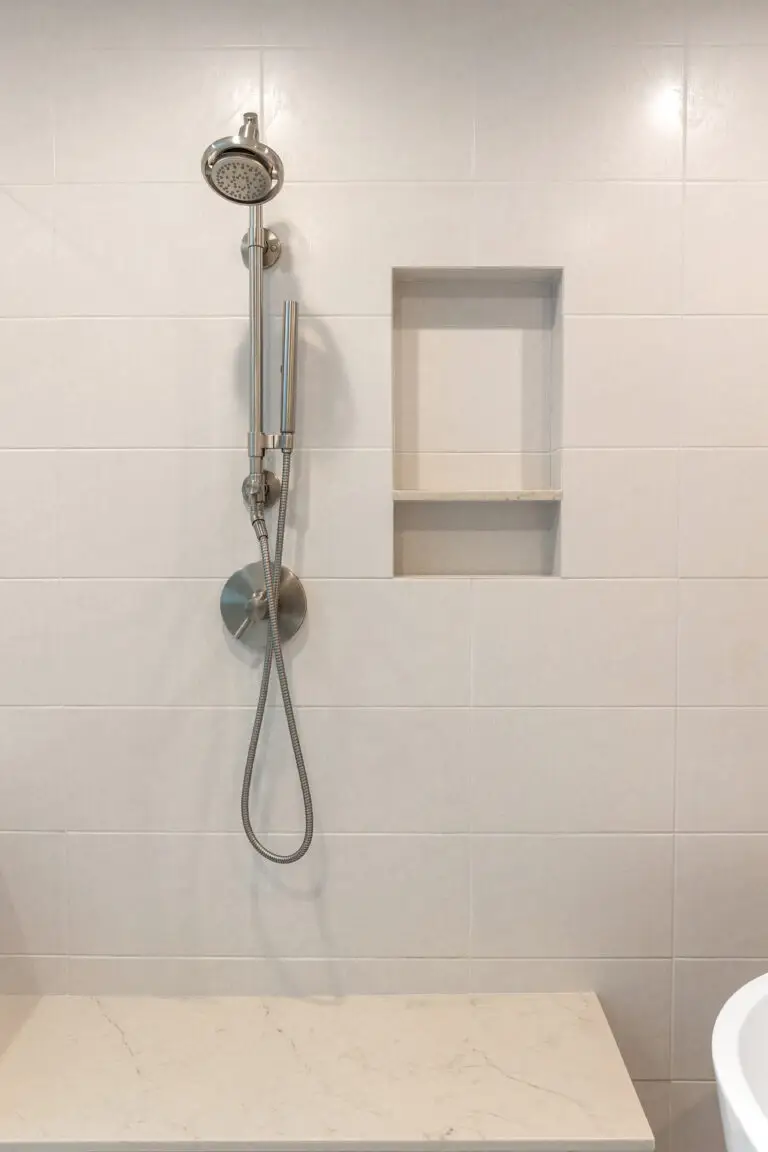 Brushed nickel slide-bar shower set beside a recessed tiled niche with quartz bench below