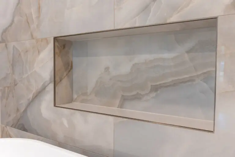 Close-up of a recessed shower niche framed in glossy marble-look porcelain tile with soft gray veining