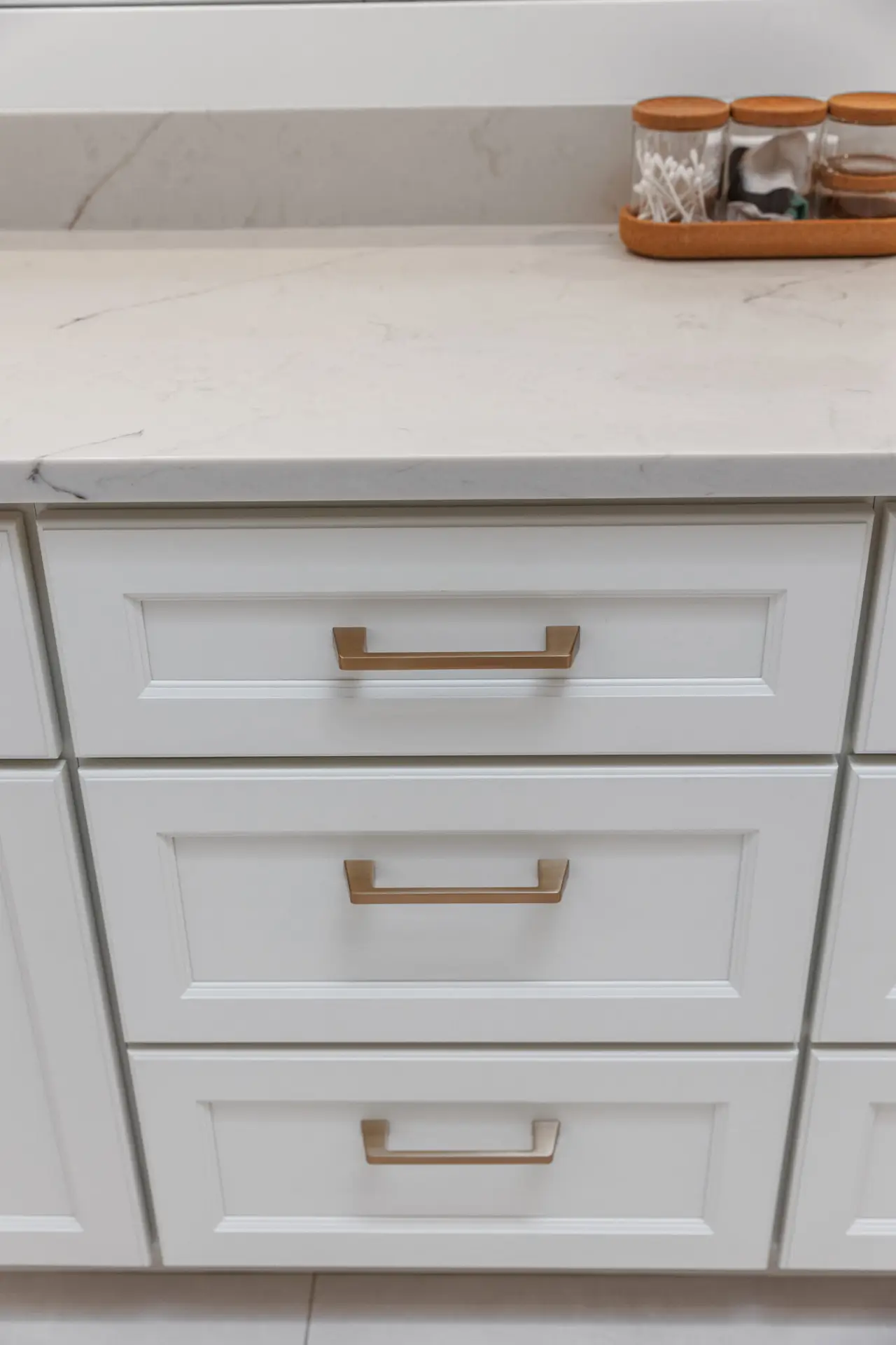 White vanity drawers with champagne bronze pulls beneath a marble-look quartz countertop