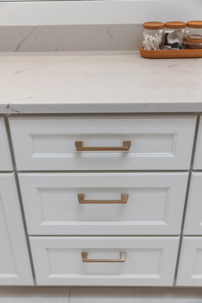 White vanity drawers with champagne bronze pulls beneath a marble-look quartz countertop