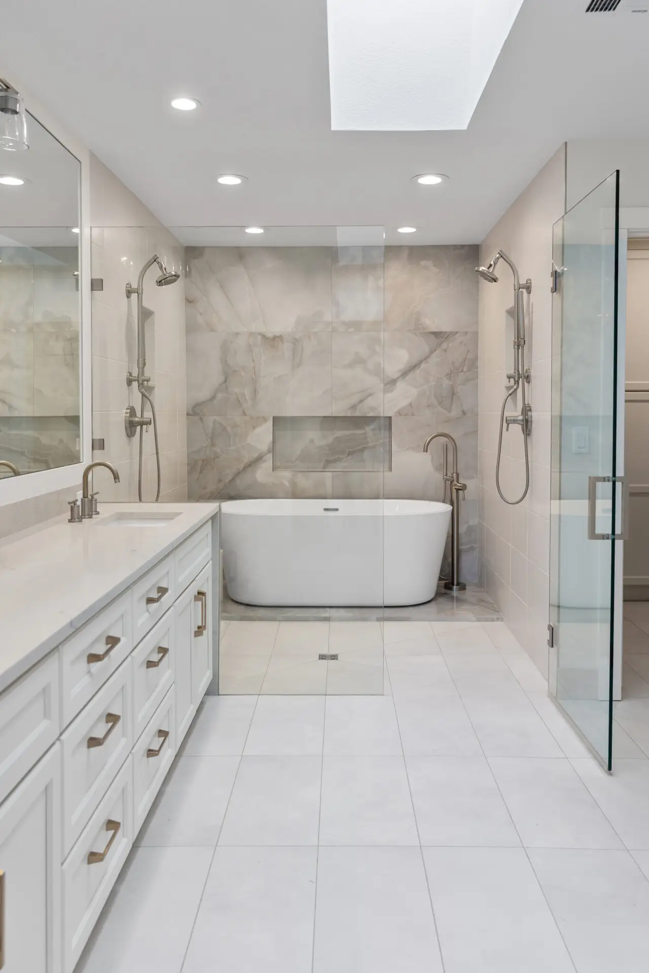 Spa-style primary bathroom with white vanity, freestanding tub, dual showers, and marble-look accent wall