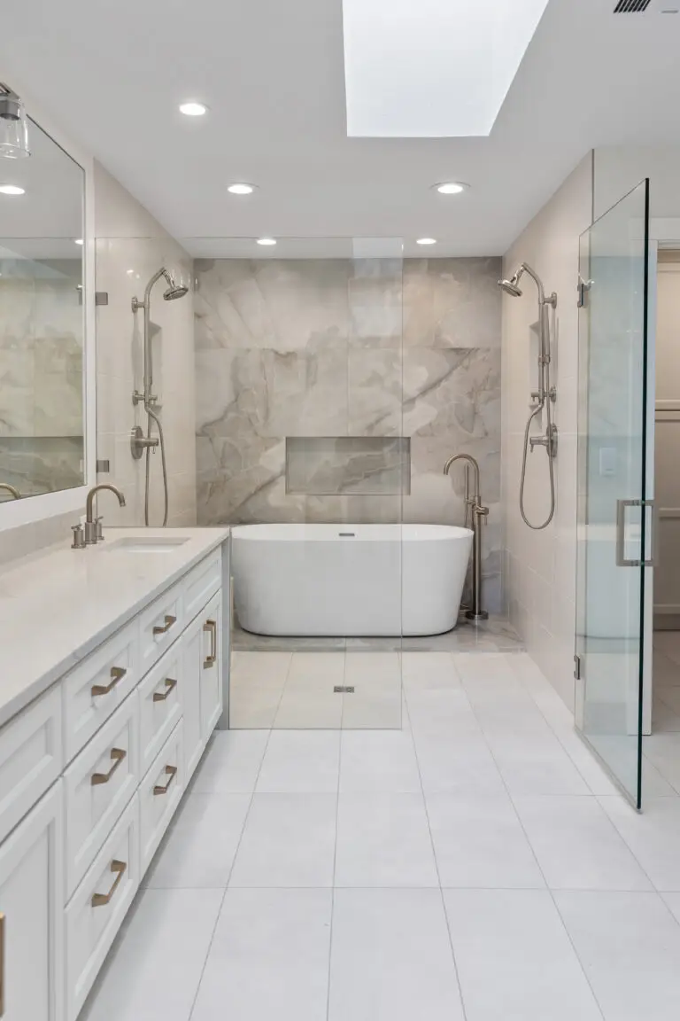 Spa-style primary bathroom with white vanity, freestanding tub, dual showers, and marble-look accent wall