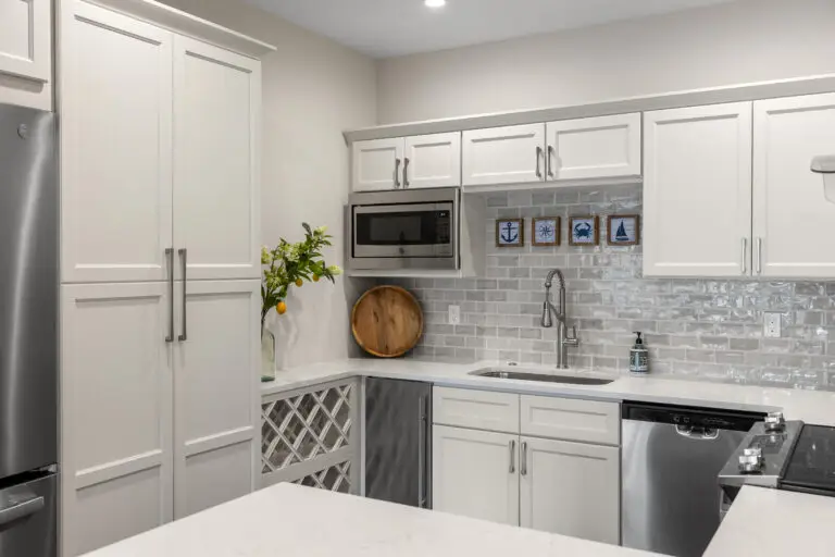 White kitchenette with gray subway tile backsplash, stainless appliances, and nautical art squares