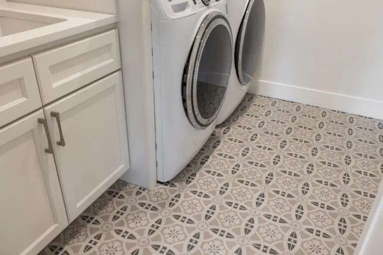 Laundry room floor in patterned beige and gray tile beside white cabinets and a front-load washer and dryer
