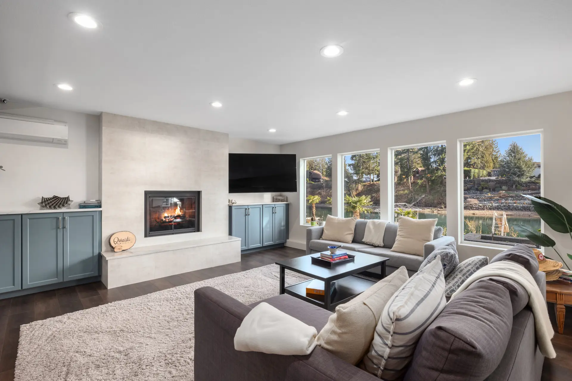 Family room with tiled fireplace, blue-gray built-in cabinets, and big windows overlooking the water