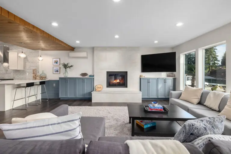 Open family room with fireplace, wall TV, blue cabinets, kitchenette bar, and wood-plank ceiling accent