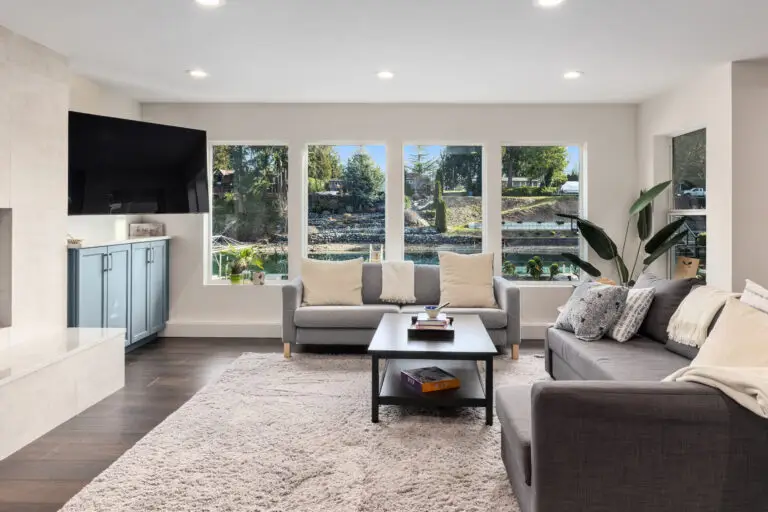 Lounge with gray sectionals, plush rug, and picture windows framing the lakeside landscape