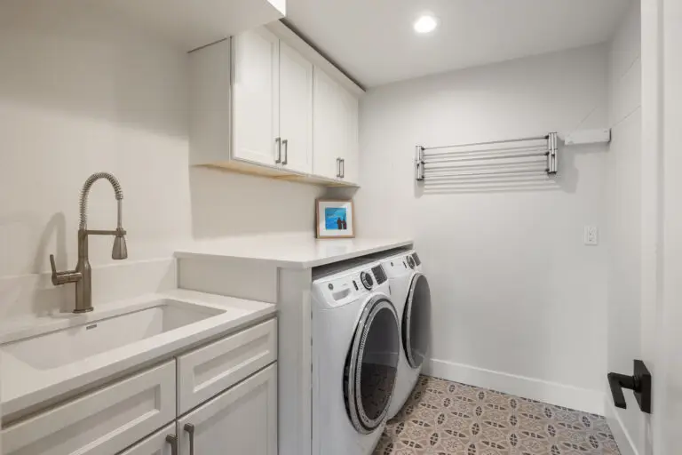 Laundry room with white cabinets, quartz folding counter over washer and dryer, utility sink, and patterned tile
