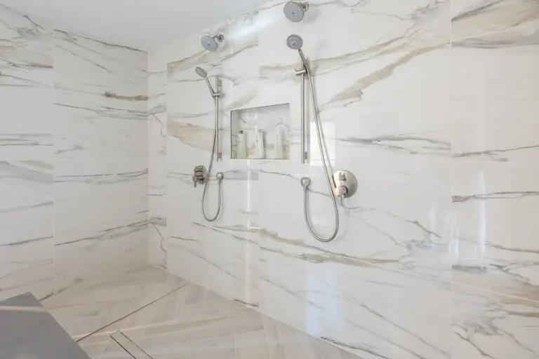 Double walk-in shower with bold marble-look walls, two handheld sprayer sets, and a gray quartz bench