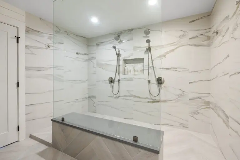 Oversized curbless shower with marble-look tile, dual shower heads, product niche, and low quartz bench