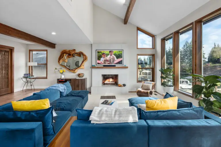 Living room with blue sectional, yellow accent pillows, TV above the fireplace, and live-edge wood mirror