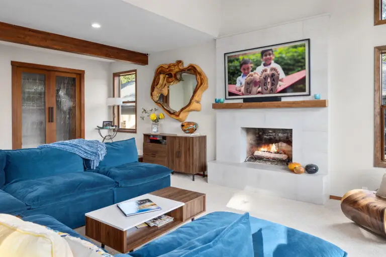 Blue velvet modular sofas around a wood coffee table facing a white tiled fireplace with rustic mantel