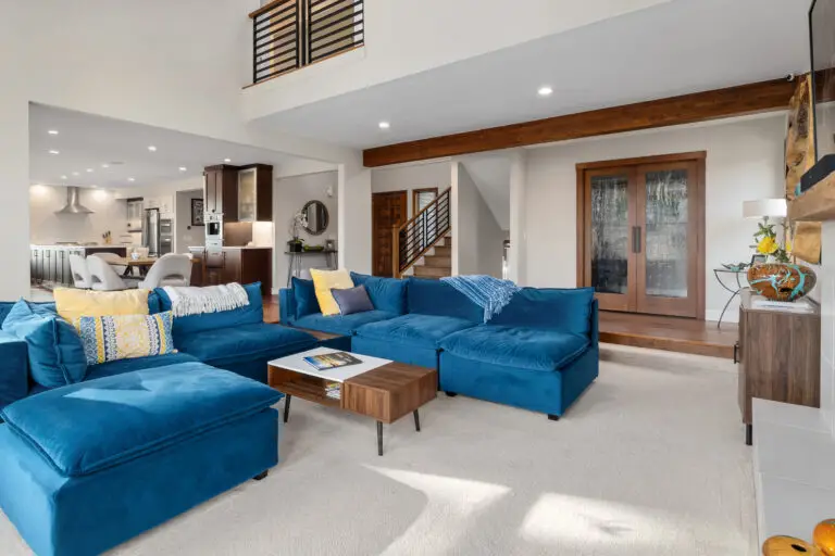 Two-story living room with blue modular sectional, stair railing above, and open kitchen in the distance