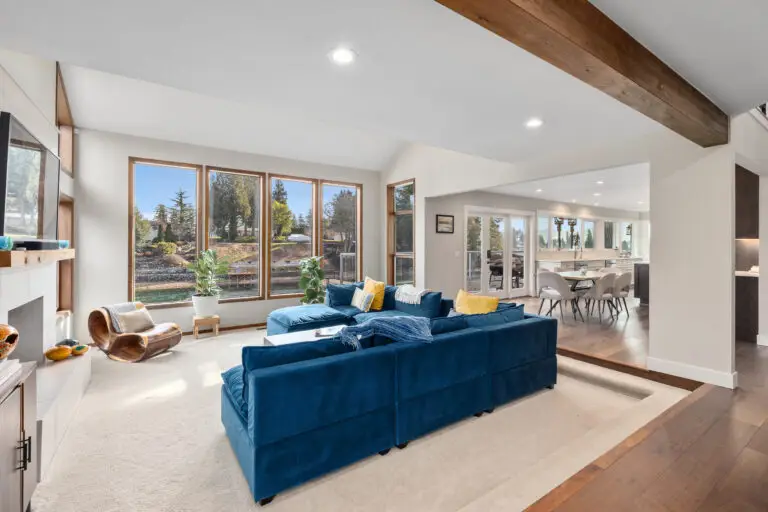 Sunken living room with blue sectional and wood beam opening to the dining area and lake-view deck doors