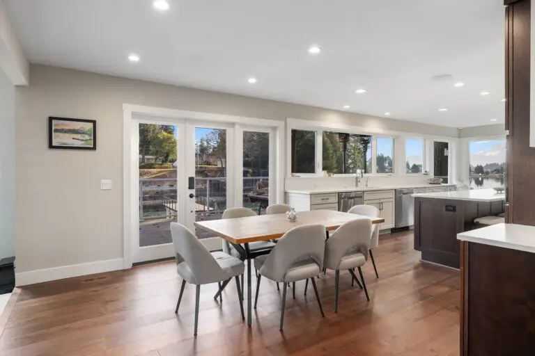 Dining area with wood-top table, upholstered chairs, and french doors leading to the waterside deck