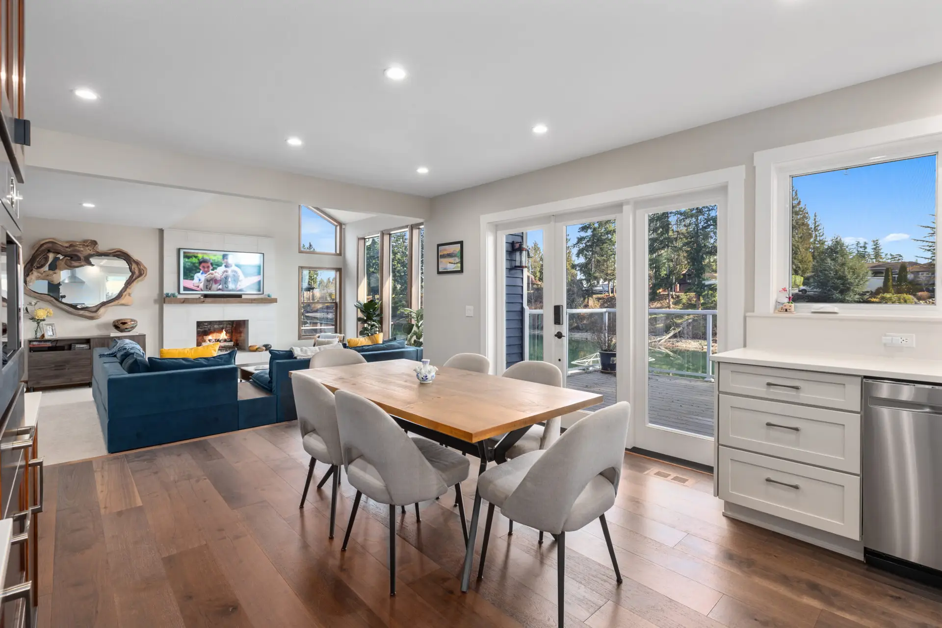 Dining room with wood table looking into the living area with blue sofas, fireplace, and water view