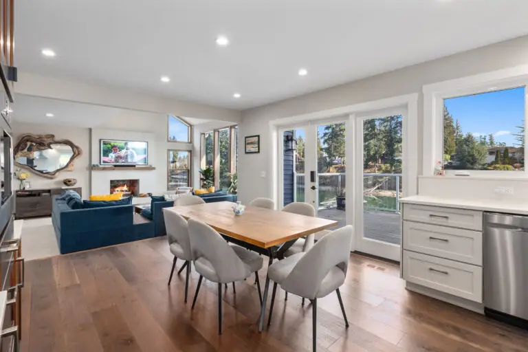 Dining room with wood table looking into the living area with blue sofas, fireplace, and water view