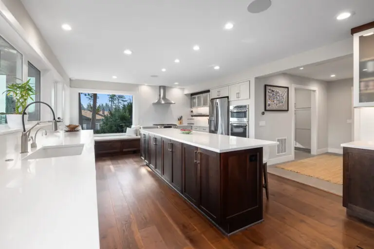Kitchen with dark wood island, white quartz counters, window seat, and stainless double ovens