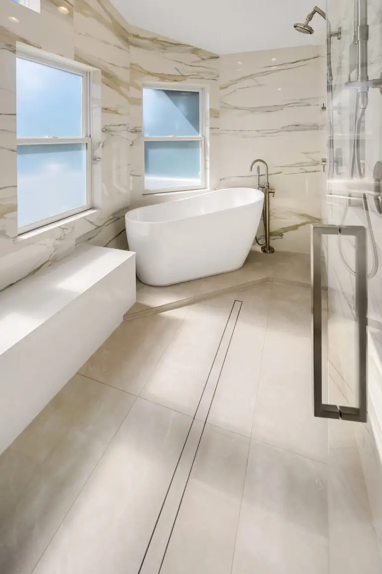 Freestanding soaker tub with floor-mounted filler, linear drain and marble-look slab walls